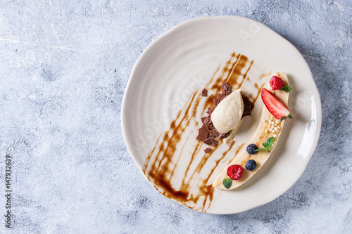 Fototapeta Food plating dessert organic banana with fresh berries, mint, chocolate rice and banana mousse served with balsamic sauce on white plate over gray texture background