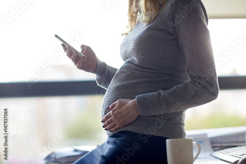 pregnant businesswoman with smartphone at office