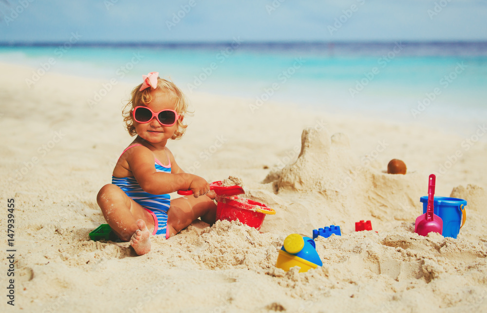 cute little girl playing with sand on beach - obrazy, fototapety, plakaty 