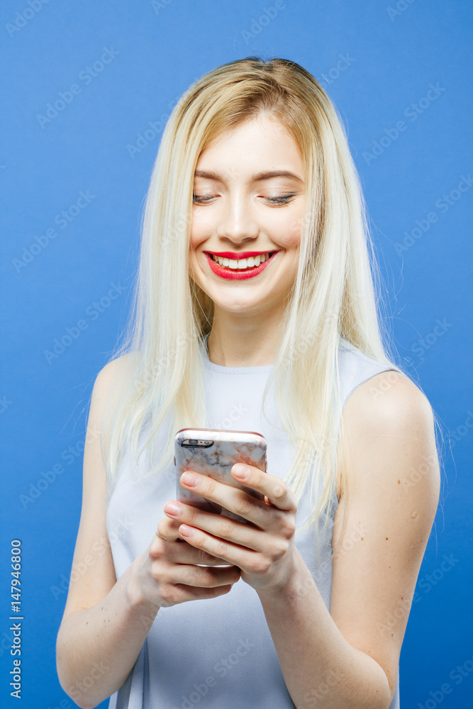 Portrait of Cute Girl with Mobile. Blonde Wearing Dress is Using her Smartphone on Blue Background in Studio. Portrait of Cute Girl with Mobile. Blonde Wearing Dress is Using her Smartphone on Blue Background in Studio.