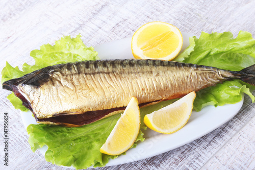 Smoked mackerele and lemon on green lettuce leaves on Wooden cutting board isolated on white background. photo