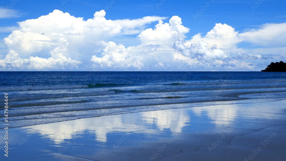 weiße Wolken spiegeln sich am blauen Meersstrand