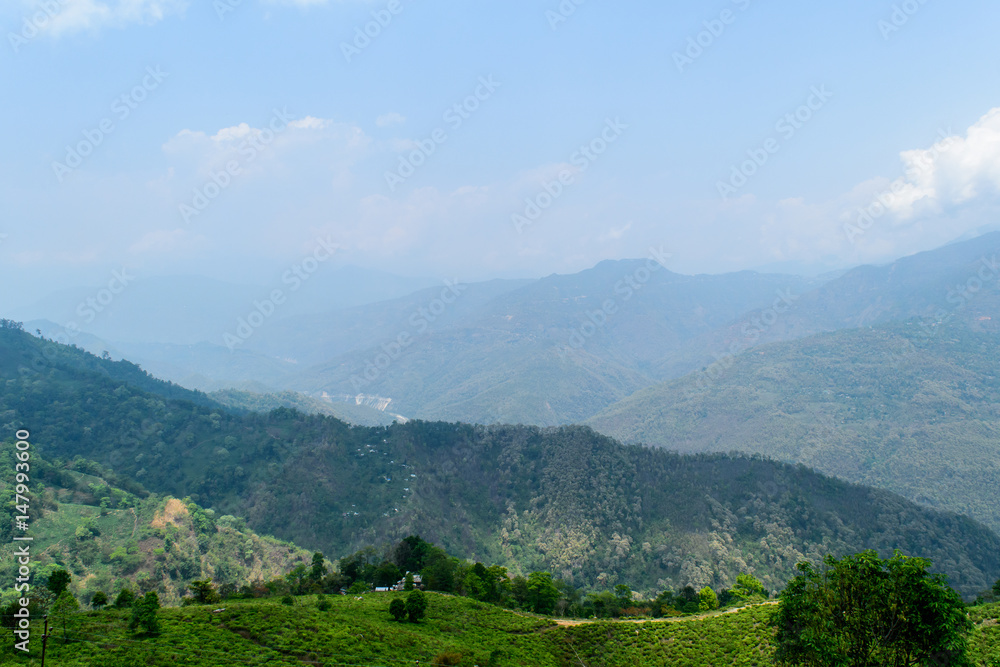 A hilltop view of mountains and blue sky with clouds on a foggy day.