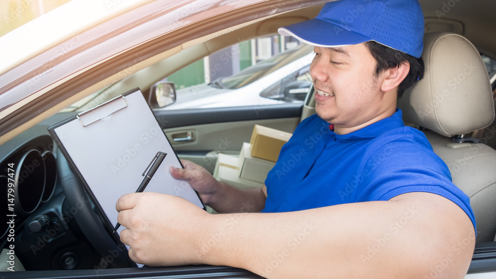 Delivery man with cardboard box checking document list In van and parcels on seat outside the warehouse Delivery man with cardboard box checking document list In van and parcels on seat outside the warehouse