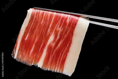 Piece of cured ham on tweezers. photo