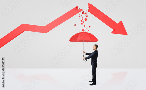 A tiny businessman hiding under a red umbrella from the rubble of a broken red statistic arrow. photo