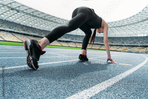 Athletic young woman in sportswear in starting position on running track stadium