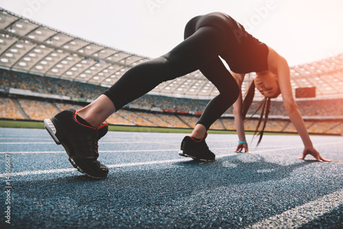 Athletic young woman in sportswear in starting position on running track stadium