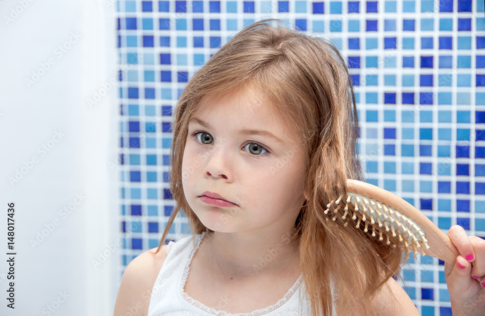 A beautiful girl is combing her hair in the bathroom. Girl got her hair tangled. The girl pouted, resentful and capricious. A beautiful girl is combing her hair in the bathroom. Girl got her hair tangled. The girl pouted, resentful and capricious.