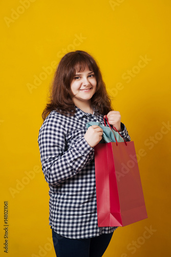Happy plus-sized woman holding colored shopping bags over yellow background.