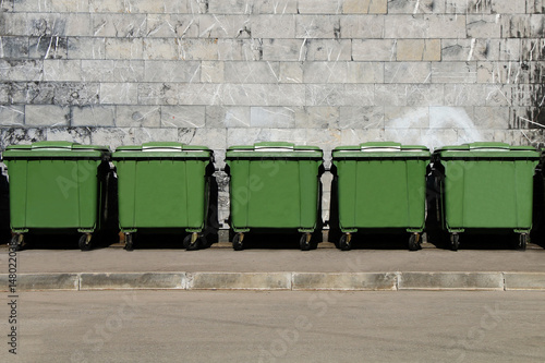 Green garbage containers standing in a row in the backyard of an industrial building.