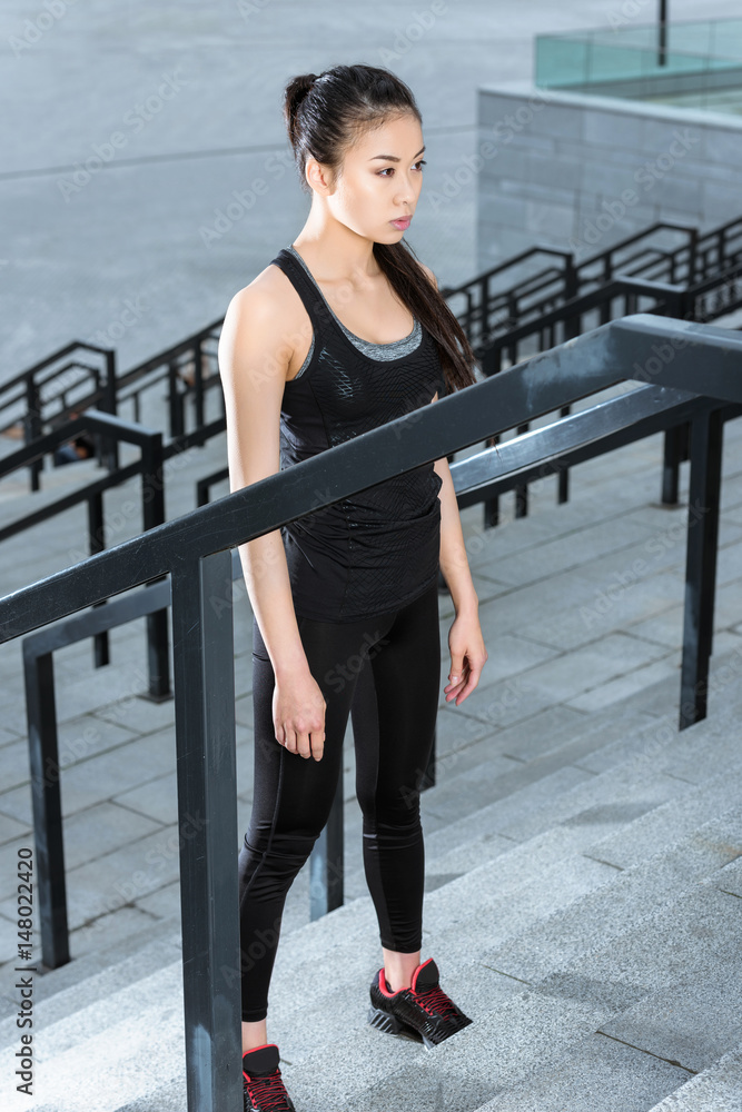 Attractive young woman in sportswear training on stadium stairs and looking away