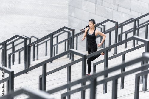 Sporty young woman in sportswear jogging on stadium stairs