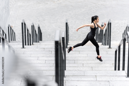 Side view of athletic young woman in sportswear running on stadium stairs