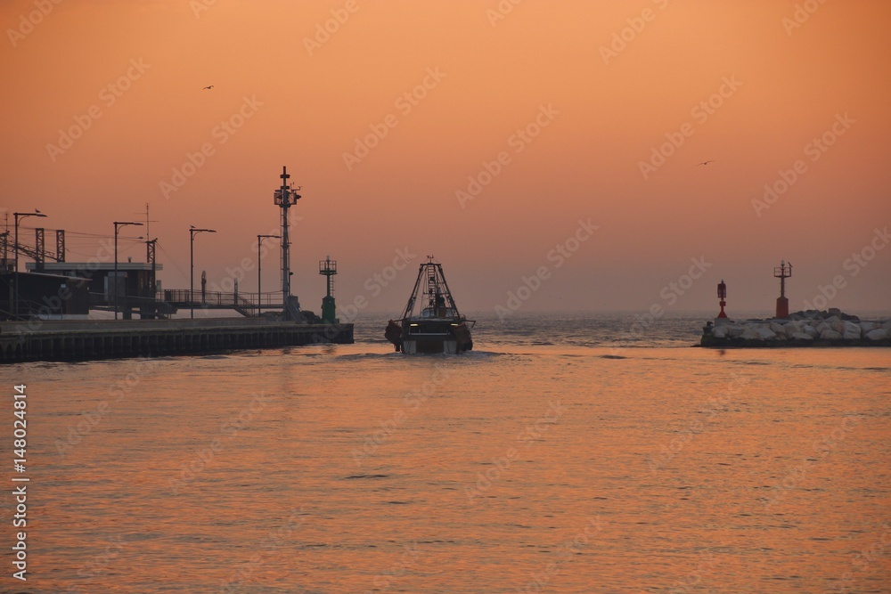 A Fishing vessel moves toward the sea at sunrise. Fishing nets on the pier in the background. Porto Garibaldi, Italy, Europe.