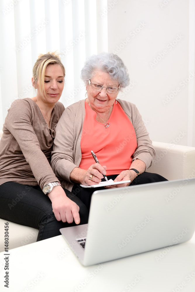attractive 40 years old woman helping with computer her mother for internet search , 80 years old senior woman at home attractive 40 years old woman helping with computer her mother for internet search , 80 years old senior woman at home