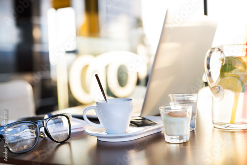Coffee cup, lemonade, eyeglasses and laptop laid on table.