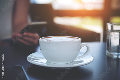 A woman using smart phone with white coffee cup on vintage wooden table with blur background