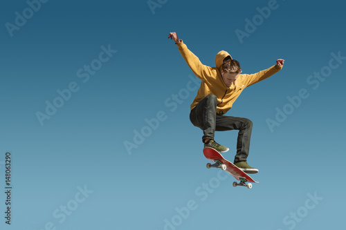 A teenager skateboarder does an ollie trick on background of blue sky gradient photo
