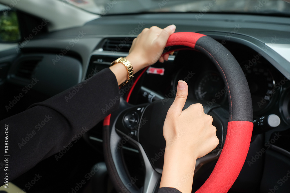 close up woman hand outstretched arms showing thumb up over car's steering wheel  for safety and assurance of driving concept.