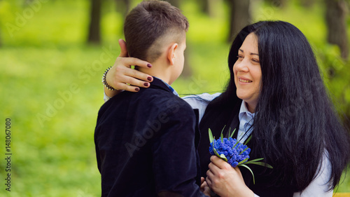 The son gives his mother a fresh bouquet of blue muscari flowers on a bench in the park. Family photo session.