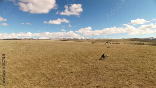 A dark suited cowboy rides his horse across an open field