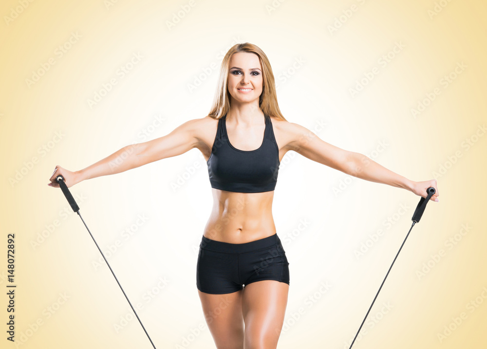 Fit, healthy and sporty woman in sportswear doing expander exercise over yellow background. Fit, healthy and sporty woman in sportswear doing expander exercise over yellow background.