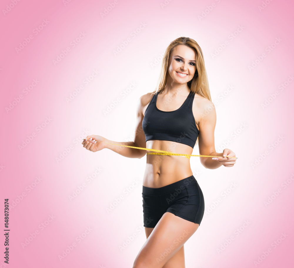 Fit, healthy and sporty woman in sportswear measuring her body over pink background. Fit, healthy and sporty woman in sportswear measuring her body over pink background.