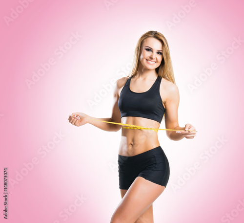 Fit, healthy and sporty woman in sportswear measuring her body over pink background. © Acronym