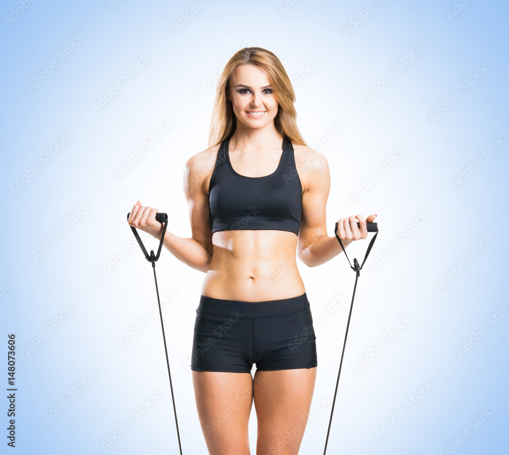 Fit, healthy and sporty woman in sportswear doing expander exercise over blue background. Fit, healthy and sporty woman in sportswear doing expander exercise over blue background.