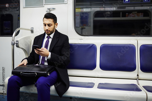 Portrait of Middle-Eastern businessman commuting to work in subway train, using smartphone to listen to music