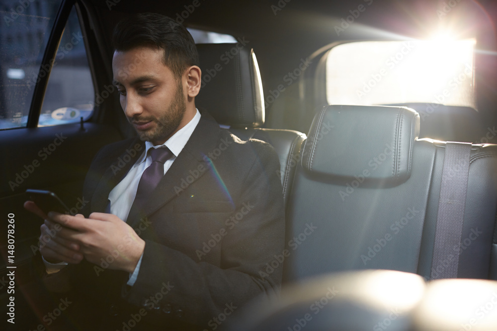 Portrait of handsome Middle-Eastern businessman using smartphone on backseat inside expensive car Portrait of handsome Middle-Eastern businessman using smartphone on backseat inside expensive car