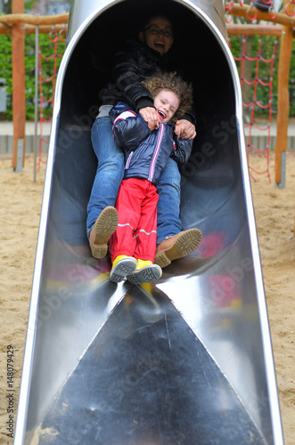 Mutter mit Kind rutschen auf einem Spielplatz eine Rutsche herunter
