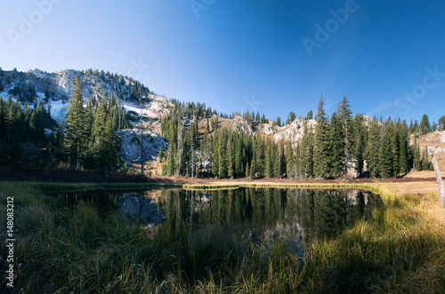 A small high mountain lake and a coniferous forest in the background of mountains with snow. Dog Lake, Uinta-Wasatch-Cache national forest. Utah, USA