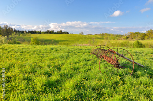 Blue sky and bright green meadow. Countryside. Sunny day. Hand plow in the foreground.