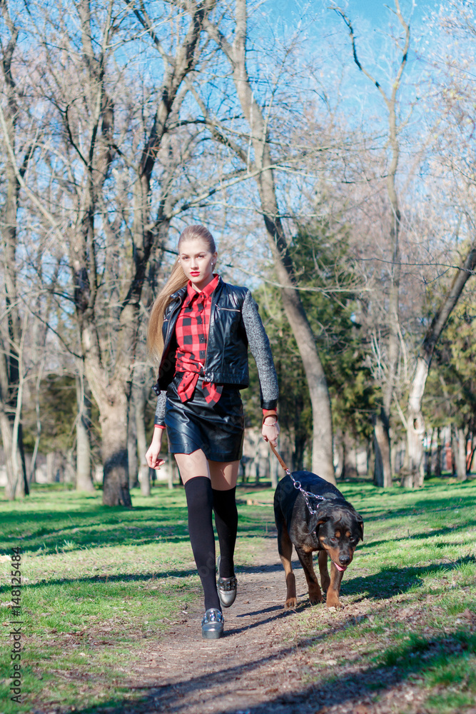 Beautiful blonde walks in the park with her dog, breeds a rottweiler, holds her by the collar Beautiful blonde walks in the park with her dog, breeds a rottweiler, holds her by the collar