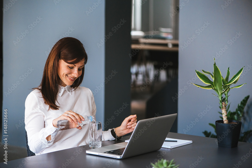 Stay hydrated. Pretty young woman in the office drinking water while working. Stay hydrated. Pretty young woman in the office drinking water while working.