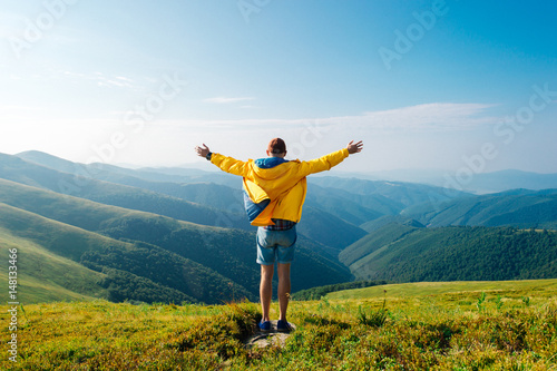 Man in yellow raincoat, jeans shorts standing at top of Carpathian mountains with view of peaks at horizon. Landscape. Nature. Valley. Travel. Freedom. Vacation. Hills. Success. Contemplation. Flight