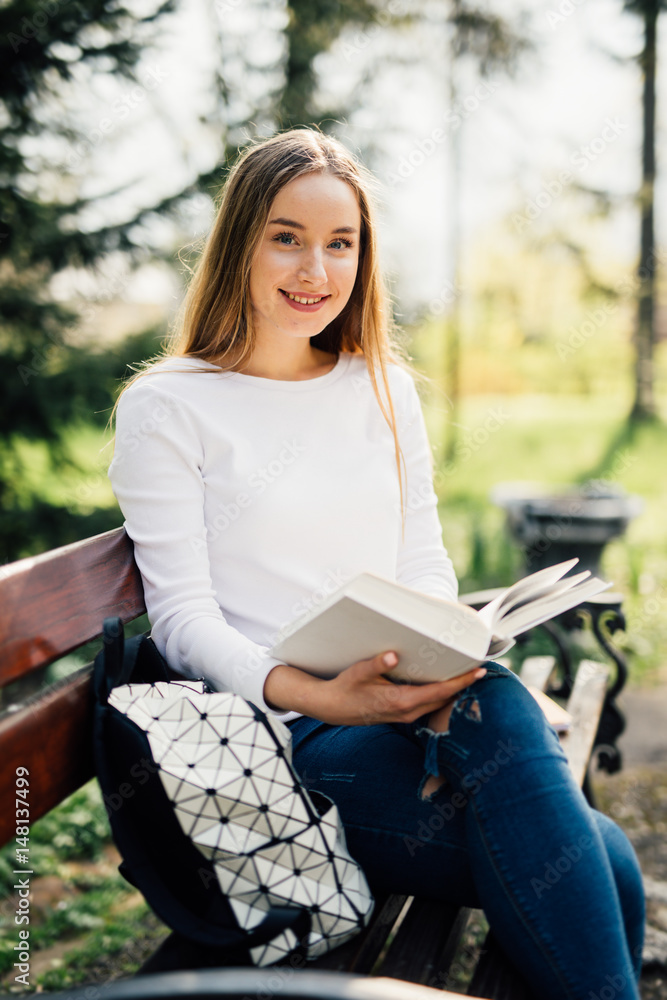 Obraz premium The student girl sitting on a bench, reading a book