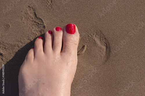 Feet of woman with nails painted red on the sand of the sea