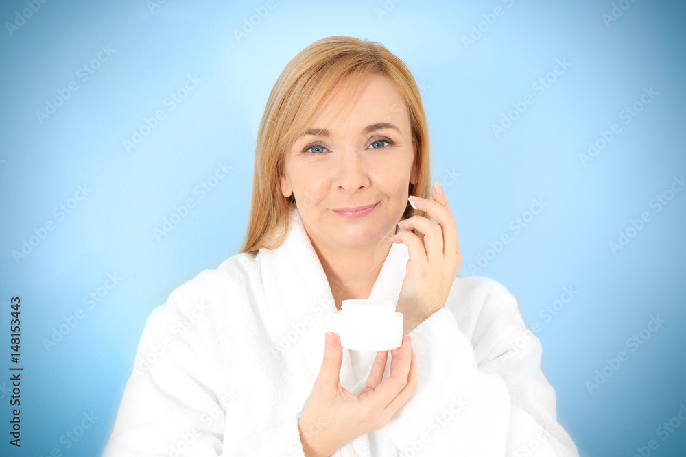 Senior woman applying anti-aging cream on face against light background Senior woman applying anti-aging cream on face against light background