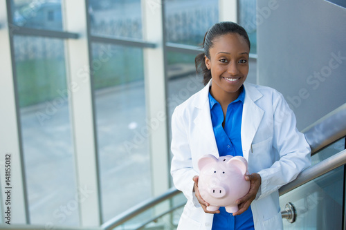 Closeup portrait, healthcare professional holding piggy bank isolated indoors clinic hospital background.  Health savings financial concept photo