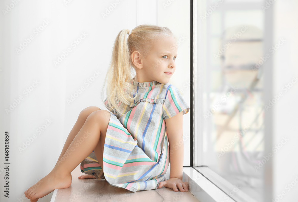Cute little girl sitting on windowsill Cute little girl sitting on windowsill