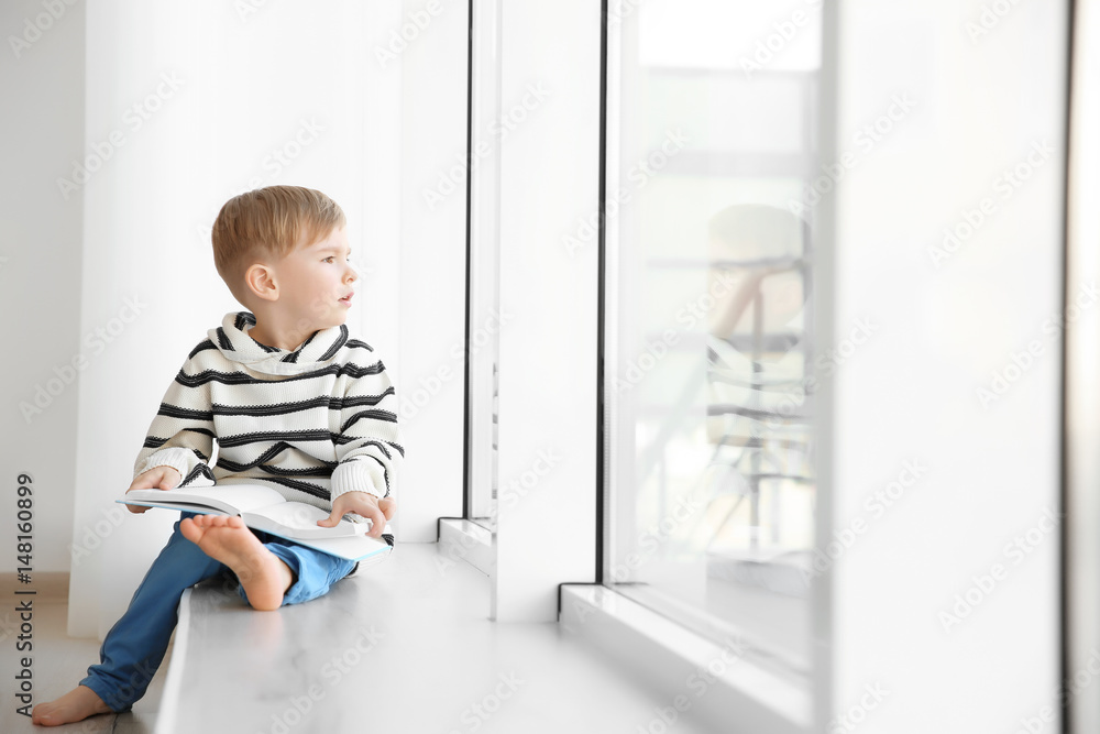 Cute little boy sitting on windowsill and reading book