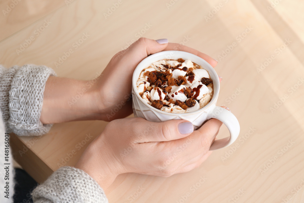 Hands of young woman and cup of tasty cocoa drink on wooden table