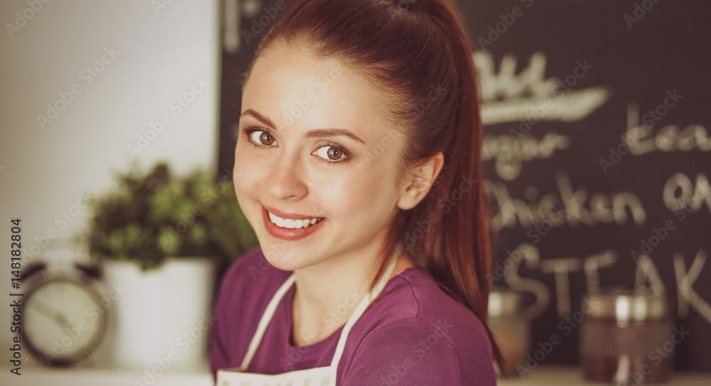 Young woman standing in her kitchen near desk