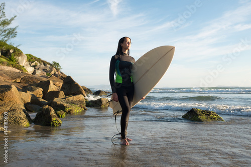 Photography Young female surfer in ocean with surfboard at rocky beach