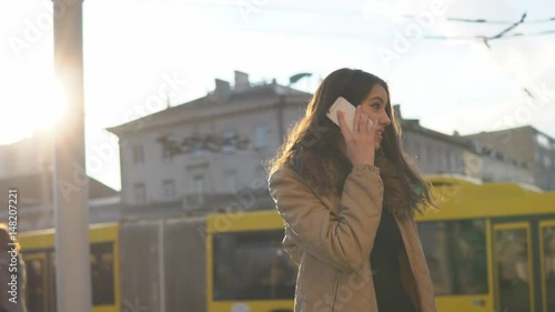 Smiling beautiful brunette woman walking at street and talking to phone photo