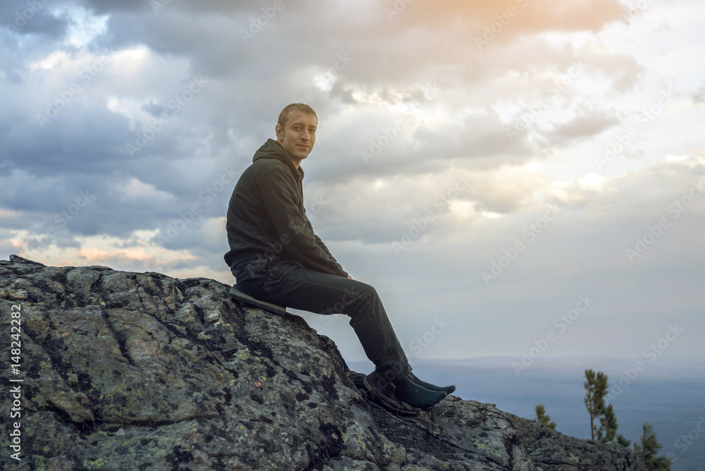Man is sitting on a stone hillside, hands looking at the view from the heights and enjoys the freedom Man is sitting on a stone hillside, hands looking at the view from the heights and enjoys the freedom