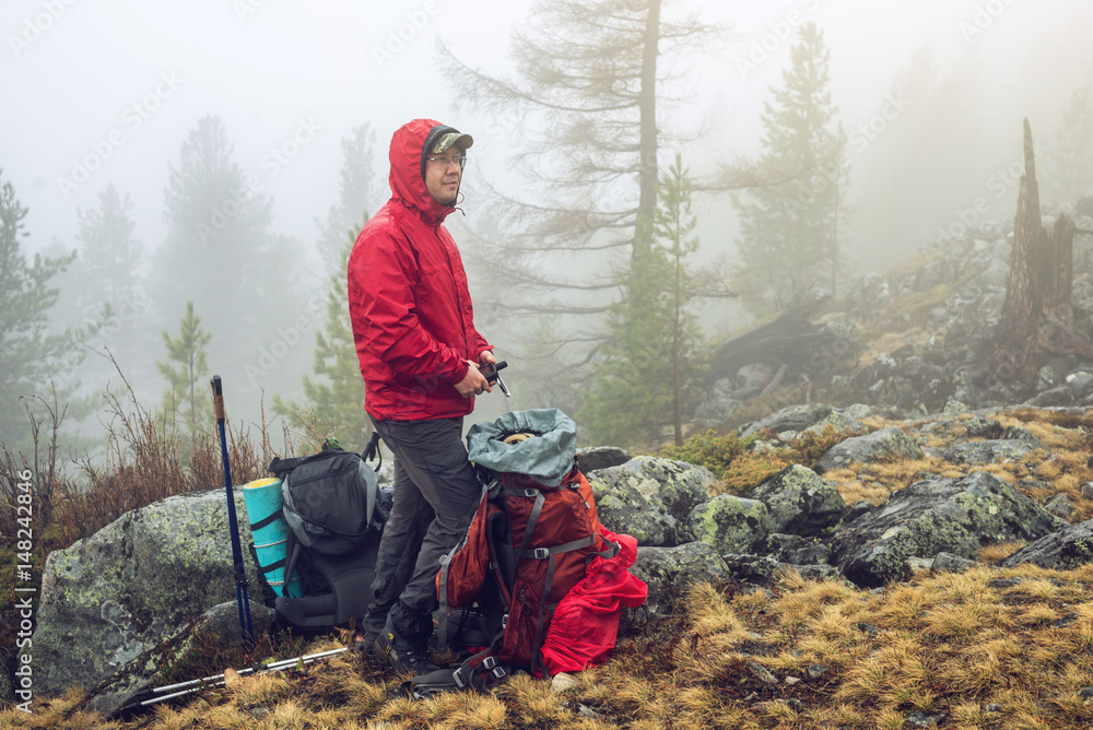 Fototapeta premium Hiker travels in the mountain forest in the mist with a backpack. Concept of travel and Hiking in wild places of nature